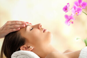 Close up  portrait of young Female Facial massage in spa. Therapist massaging woman’s head against bright colorful background.