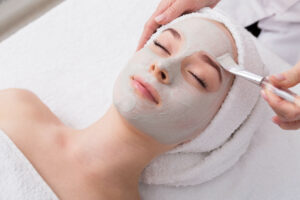 Woman gets face mask by beautician at spa Face peeling mask, spa beauty treatment, skincare. Woman getting facial care by beautician at spa salon, side view, close-up